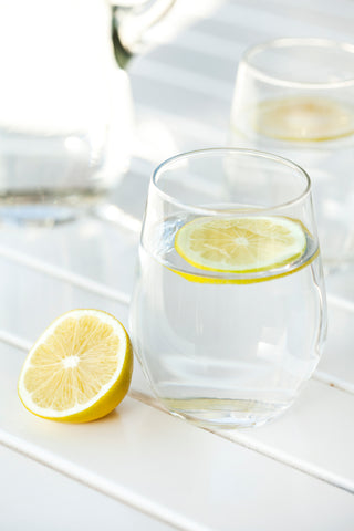 Clear glass of water with a slice of lemon floating on top and a cut lemon beside it