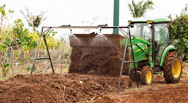 farmer on green tractor turning organic compost pile on noni farm kauai